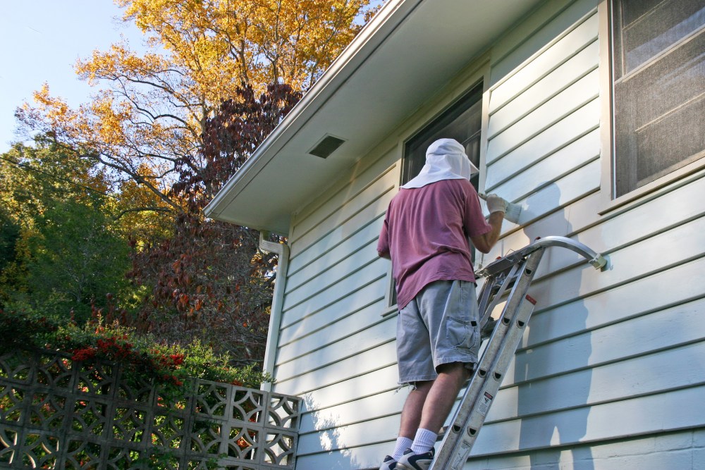 Man On Ladder Paints a House Exterior